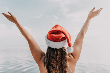 A woman wearing a red Santa hat is holding her hands together in a heart shape over the water.の写真素材
