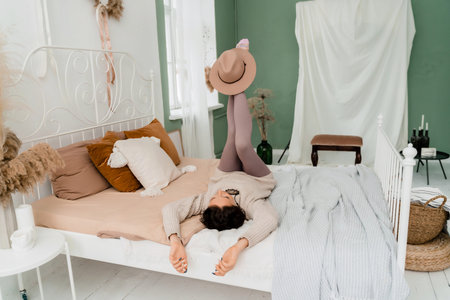 Lifestyle concept. A young middle-aged woman in a sweater lies on the bed on her back, laughs and...