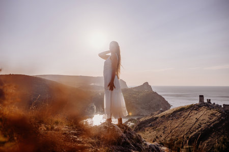 woman stands on a hill overlooking the ocean, her arms raised in the air. Concept of freedom and joy, as if the woman is celebrating a moment of happiness or accomplishment.の写真素材