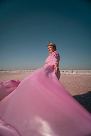 A woman in a pink dress stands on a pink sandy beach with a blue sky in the background.の写真素材