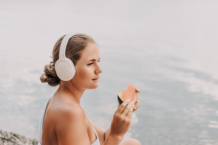 A woman is eating a watermelon slice. The watermelon is pink and green. The woman is smiling as she eats the fruit.の写真素材