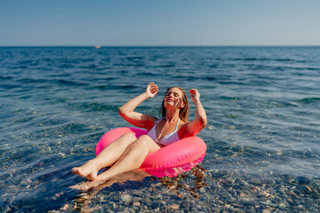 A woman is floating on a pink inflatable raft in the ocean