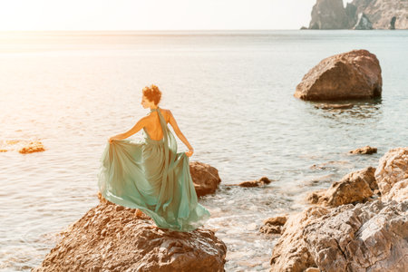 Woman in a long mint dress posing on a beach with rocks on sunny day. Girl on the nature on blue sky background.の写真素材