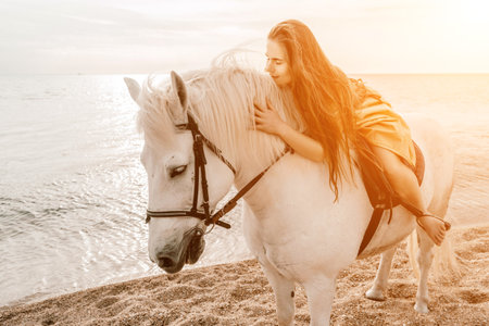 A woman stands next to a white horse on a beach, with the blue sky and sea in the background.の写真素材