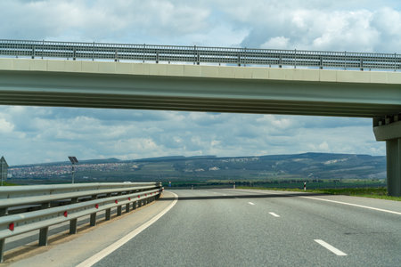 A bridge spans a road with a clear sky above. The bridge is a large structure that is visible from a...