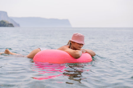 A woman is laying on a pink inflatable raft in the ocean. The scene is peaceful and relaxing, with the woman enjoying the water and the sun.の写真素材