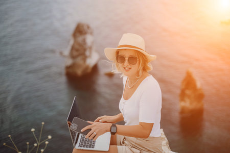 Freelance women sea working on the computer. Good looking middle aged woman typing on a laptop keyboard outdoors with a beautiful sea view. The concept of remote work.の写真素材