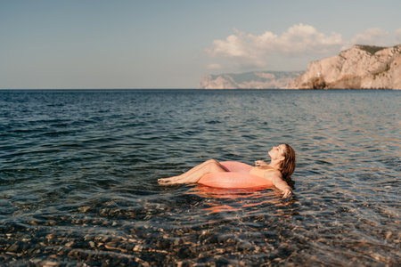 A woman is floating on a pink inflatable raft in the ocean. The water is calm and the sky is clear. The woman is enjoying her time in the water.の写真素材