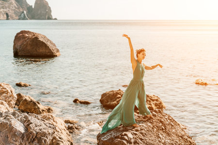 Woman green dress sea. Woman in a long mint dress posing on a beach with rocks on sunny day. Girl on the nature on blue sky background.の写真素材