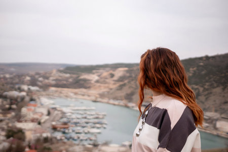 A woman is sitting on a rock overlooking a body of water. The scene is peaceful and serene, with the woman looking out over the water and taking in the view.の写真素材