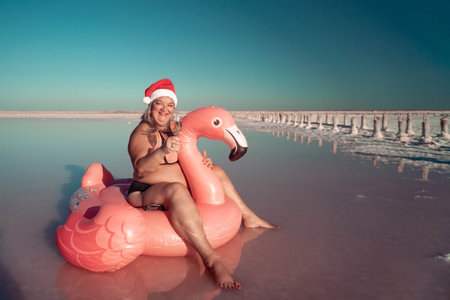 Santa Flamingo Christmas woman Riding Inflatable Flamingo Pink Lake. A woman wearing a Santa hat sits on a pink flamingo float in a body of water. He is smiling.の写真素材