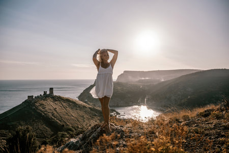 A blonde woman stands on a hill overlooking the ocean. She is wearing a white dress and she is enjoying the view.の写真素材