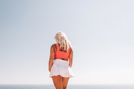A woman is standing on a cliff overlooking the ocean. She is smiling and she is happy.の写真素材