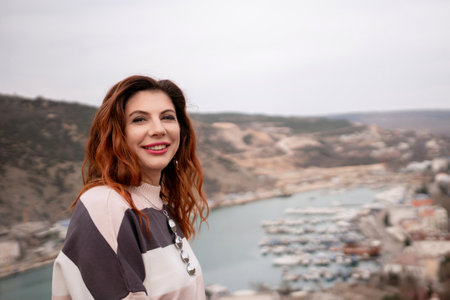 A woman is sitting on a rock overlooking a body of water. The scene is peaceful and serene, with the woman looking out over the water and taking in the view.の写真素材