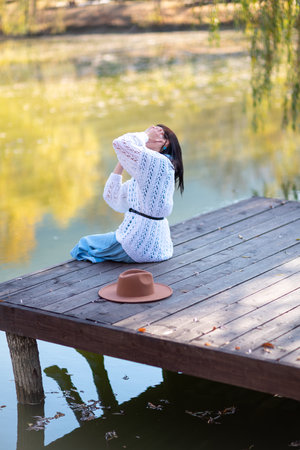 Autumn lake woman. She sits by a pond on a wooden pier in autumn and admires nature. The concept of tourism, weekends outside the city.の写真素材