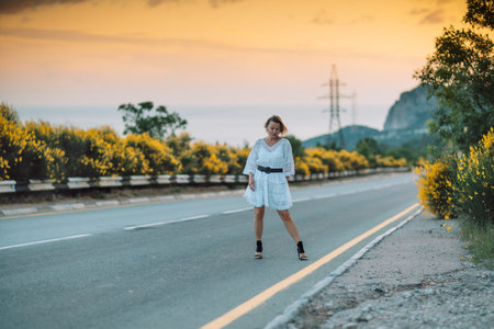 A woman in a white dress is walking on a road near a yellow bushの写真素材