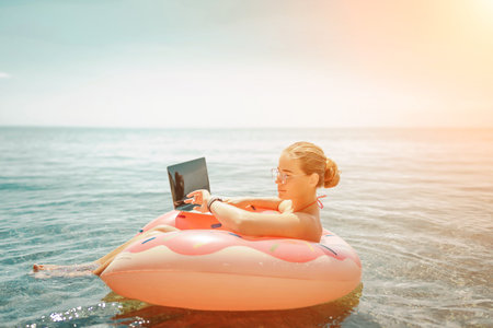 Woman laptop sea. Freelancer woman in sunglases floating on an inflatable big pink donut with a...