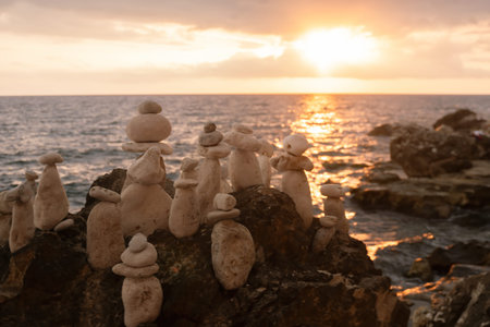 Stone Towers Sunset Ocean - A group of balanced stone towers on a rocky beach at sunset with the sun...