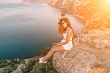 Happy woman in white shorts and T-shirt, with long hair, talking on the phone while enjoying the scenic view of the sea in the background.の写真素材