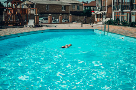 A woman is swimming in a pool. The pool is surrounded by a fence and has a playground in the...