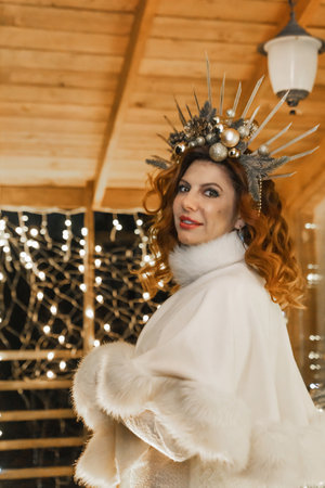 Woman Crown Fur Winter Wonderland - Portrait of a woman wearing a crown and a fur coat, looking towards the camera, with a wooden background adorned with christmas lights.の写真素材