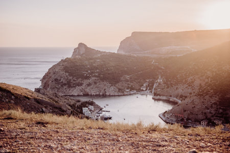 A beautiful sunset over a mountain with a small town in the distance. The sun is setting behind the mountains, casting a warm glow over the landscape. The water in the valley is calm and peaceful.の写真素材
