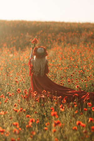 A woman in a red dress is standing in a field of red flowersの写真素材