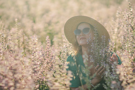 Woman Hat Flowers: Summer field, serene woman in straw hat enjoys pink flowers; peaceful nature scene.の写真素材