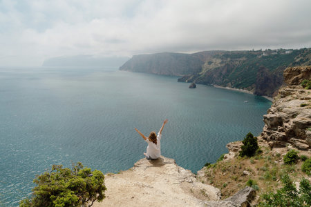 A woman is sitting on a rock overlooking the ocean. She is smiling and she is enjoying the view.の写真素材
