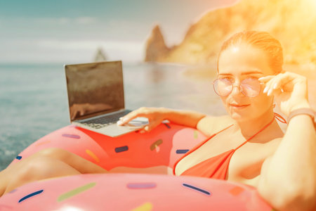 Woman laptop sea. Freelancer woman in sunglases floating on an inflatable big pink donut with a laptop in the sea. People summer vacation rest lifestyle conceptの写真素材