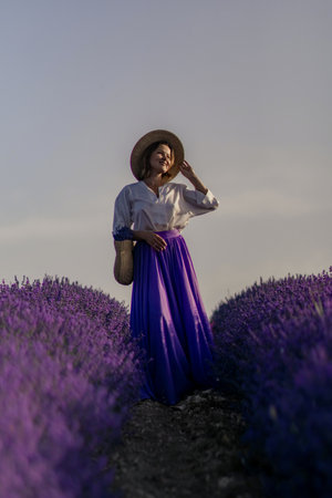 A woman wearing a straw hat and a purple skirt stands in a field of lavenderの写真素材