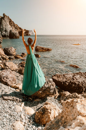 Woman green dress sea. Woman in a long mint dress posing on a beach with rocks on sunny day. Girl on the nature on blue sky background.の写真素材