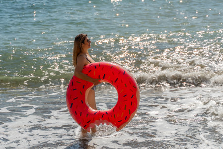 Woman Beach Inflatable Float Summer Vacation - A woman stands in the shallows of the ocean holding an inflatable float.の写真素材