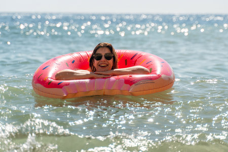 Woman Float Ocean - Smiling woman floats on a red inflatable ring in the ocean on a sunny day.の写真素材