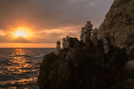 Group of stone figures on a cliff watching the sunset over the ocean.の写真素材