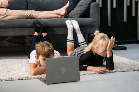 Kids Laptop Home - Two children using a laptop while lying on the floor in a living room.の写真素材