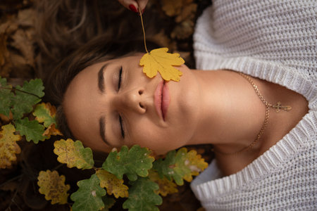 Woman Autumn Leaves Relaxation: Peaceful autumn scene, young woman lying on fallen leaves, enjoying natures beauty.の写真素材