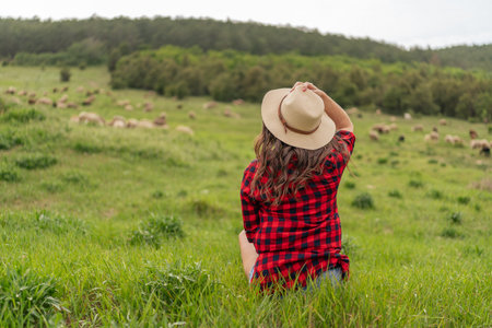 A woman wearing a straw hat sits in a field of grassの写真素材
