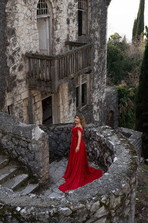 Woman Red Dress Castle Ruin: Romantic photoshoot near ancient stone building, showcasing elegance and decay.の写真素材