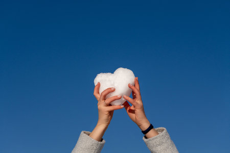 Heart Hands Sky: White heart held aloft outdoors, sunny day, symbolizing love or hope.の写真素材