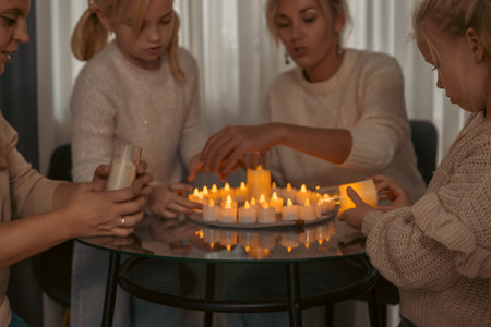 Candles Family Home Lighting: Women and girls light numerous LED candles together on a glass table indoors, creating a warm, festive atmosphere.の写真素材
