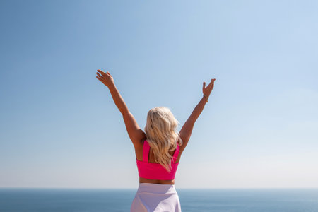 A woman in a pink top and white skirt is standing on a cliff overlooking the ocean. She is smiling and she is happy.の写真素材