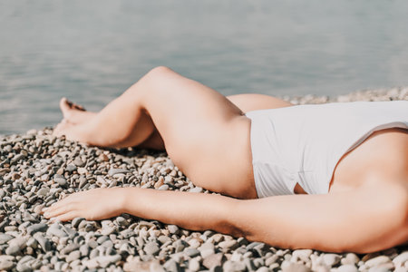 A woman is laying on the beach. She is wearing a white bikini top and white bikini bottoms.の写真素材