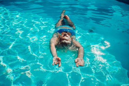 Woman relaxing swimming pool. Happy woman in a blue swimsuit floating in the pool, look form aboveの写真素材