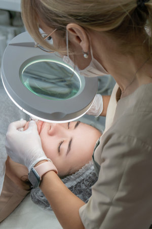 Cosmetology Clinic Face Treatment Procedure: Professional dermatologist performs facial treatment using magnifying lamp.の写真素材