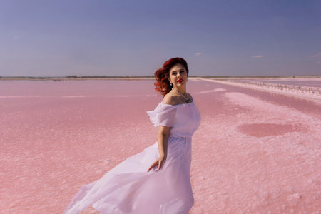 Woman Pink Lake Dress - A woman in a white dress stands on a pink salt lake.の写真素材