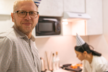 Chef Man Kitchen Cooking: Middle-aged man smiles near chef preparing food in modern kitchen. Event possibly culinary class or demonstration.の写真素材