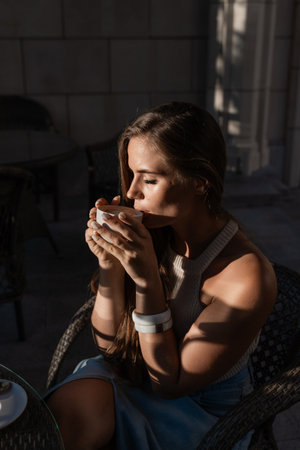 Woman Coffee Cafe - A woman is sitting at an outdoor cafe table, enjoying a cup of coffee. The photo captures the warm sunlight illuminating the scene.の写真素材