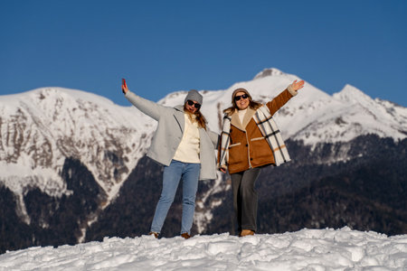 Women Mountains Winter: Joyful friends pose atop snowy mountain peak, celebrating winter adventure.の写真素材