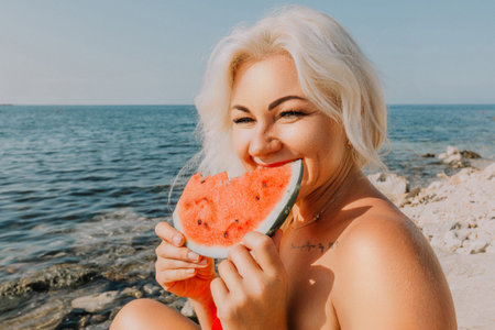 Watermelon Beach Summer: Woman enjoys refreshing watermelon slice on sunny beach during summer vacation.の写真素材